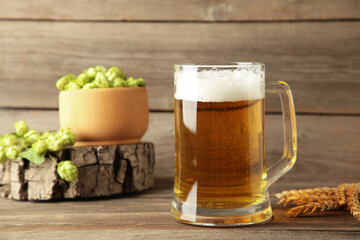 Glass of fresh beer with green hops and wheat on a grey background