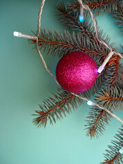 On the Christmas tree there is a shiny round pink Christmas toy on a turquoise background with garlands . top view . Christmas