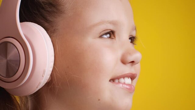 Music for kids. Close up portrait of cute smiling little girl wearing pink headset opening her eyes and looking aside