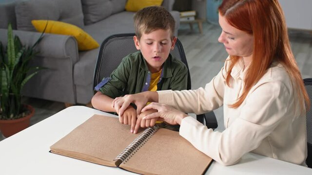 invalid child learns to read braille, female pedagogue helps blind kid move his fingers through the letters