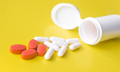 White and red pills are poured from a jar on a yellow background. Food supplement, multivitamins, medications. treatment and prevention of diseases, therapy. wellness