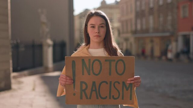 Woman holding No to racism banner on city street