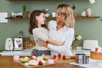 Obraz na płótnie Canvas Happy chef cook baker mom woman in white shirt work with child baby girl helper hug each other at kitchen table home Cooking food process concept Mommy little kid daughter prepare fruit sweet cake