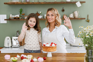 Excited chef cook baker mom woman in white shirt work with baby girl helper show okay gesture at kitchen table home Cooking food process concept. Mommy little kid daughter prepare fruit sweet cake