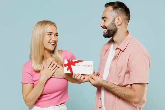 Young smiling happy couple two friends family man woman in casual clothes hold give gift certificate coupon voucher card for store together isolated on pastel plain light blue color background studio.