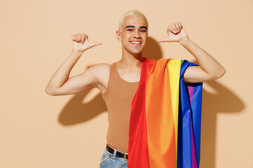 Young cool blond latin gay man with make up in beige tank shirt with rainbow flag on shoulder point...