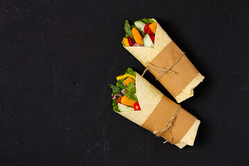 Tortilla wraps, with breaded chicken sticks with vegetables, burritos, on a black background, ...