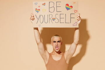 Young activist blond latin gay man with make up in beige tank shirt hold card sign with be yourself...