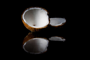 Coconut on a black background, with reflection. Two halves of a broken coconut.