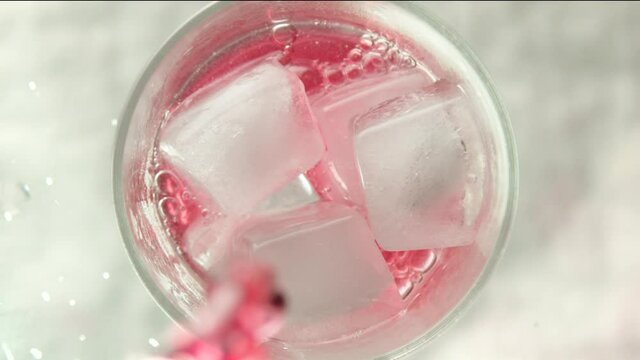 Raspberry lemonade is poured into a glass with ice on a light background
