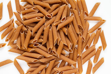 Whole grain Penne pasta pieces, raw, uncooked. Penne rigate type (furrowed), with ridged surface. Composition on white background.