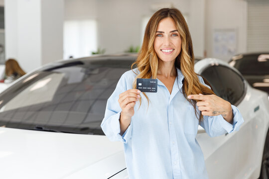 Happy woman customer buyer client in blue shirt hold showing credit bank card choose auto want to buy new automobile in car showroom vehicle salon dealership store motor show indoor. Sales concept