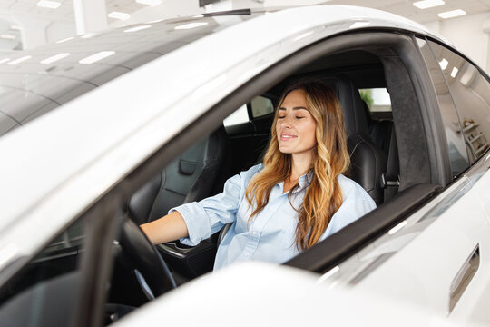 Relaxed woman customer buyer client in blue shirt hold put hands on steering wheel with close eyes choose auto want buy new automobile in car showroom vehicle salon dealership store motor show indoor