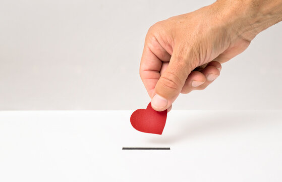 Red heart symbol is put by person's hand into slot of white donation box