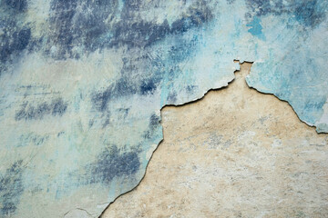 Wall of old building with partially fallen off plaster in gray and blue colors. Space is divided into two parts of different structures. Abstract background. Copy space. Close-up. Selective focus.