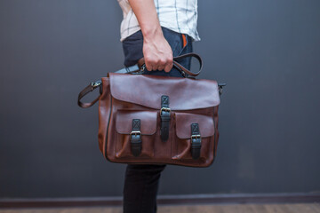Man holding brown leather messenger bag in the hand