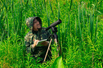 birdwatcher records the results of the observations while standing among the tall grass in the...
