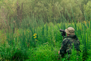 male birdwatcher makes observations in the wild with a spotting scope standing among the tall grass