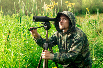 birdwatcher with a spotting scope and notepad among the tall grass in the valley