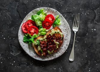 Delicious brunch - avocado, bacon sandwich and tomato lettuce salad on a dark background, top view