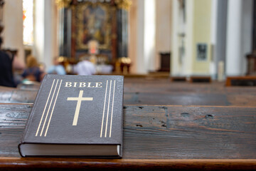 The Bible on the table of a prayer bench in the church with a altar.