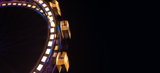 Naklejka premium Ferris wheel entertainment object in amusement park at night long exposure circle motion festive lighting on black background empty copy space for your text here of advertising panoramic