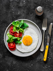 Breakfast plate - fried egg, bacon and vegetables salad on a dark background, top view
