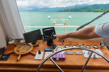 Vista del interior de una embarcación con pantallas y herramientas para la navegación  y la mano del capitán - obrazy, fototapety, plakaty