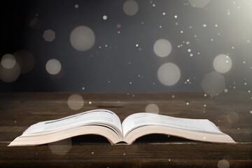 Open old book on wooden table and dark background with shine and flying particles