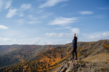 Fototapeta premium A young girl stands on the edge of a cliff with a magnificent view and looks at it, her arms spread wide.