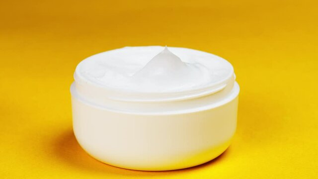 Female hand taking moisturizing cream for face or body on yellow background. Bowl with soft cream close-up, cosmetic texture. Beauty and health, skin care concept.