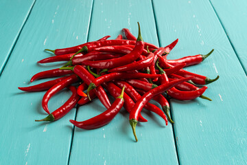 Heap of red hot chili peppers on a turquoise wooden table. Raw spicy chilli pepper pods close-up. Whole fresh pungent chiles for cooking. Bitter spice ingredient for meat dishes. Front view.