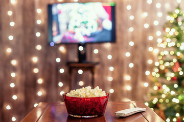 Christmas eve. Red bowl with popcorn. Remote control for tv on the table. Home cinema. Cropped, close up