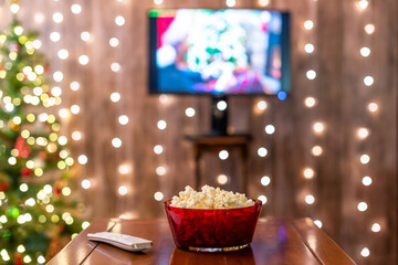 Christmas eve. Red bowl with popcorn. Remote control for tv on the table. Home cinema. Cropped, close up - 458094627