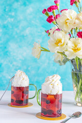 Two desserts on the table. Summer dessert: jelly with raspberries and blueberries, decorated with whipped cream. Summer snack and a bouquet of flowers in a vase.