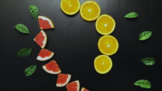 Stop motion video fruit. Slices of grapefruit and orange move and swirl against a black background with green mint leaves. Bright colorful animation. 4K
