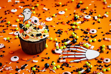 halloween cupcake ghost bone hand colored sprinkles on a colorful orange background