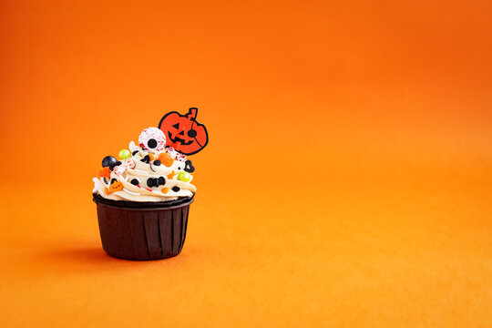 halloween cupcake decored with Jack O'Lantern colored sprinkles on a colorful orange background