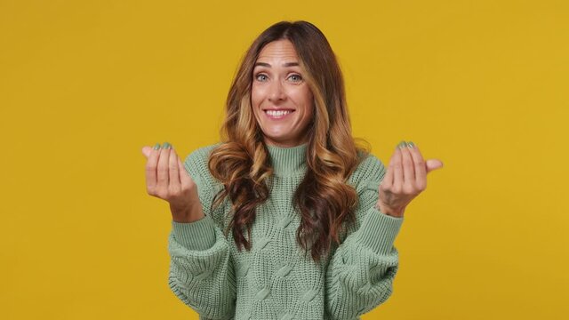 Amazing cheerful young brunette woman 30s years old wears mint sweater looking camera rubbing fingers showing cash gesture ask for give me money beg isolated on plain yellow background studio portrait