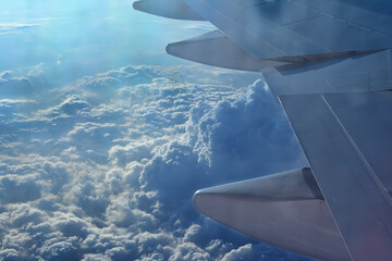 Part of an airplane wing and clouds below. View from the plane