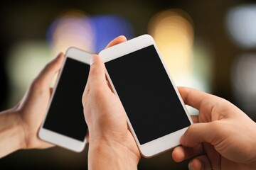 Two modern smartphones with blank screens in human hands