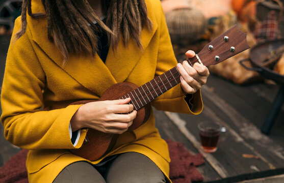 girl with dreadlocks closeup playing an acoustic instrument ukulele in autumn on the terrace