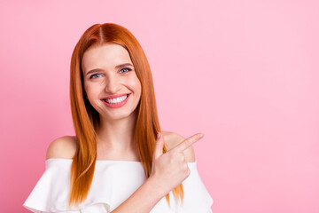 Portrait of attractive cheerful red-haired girl showing copy space ad new offer isolated over pink pastel color background