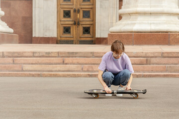 brunette teen with glasses with a skateboard on the streets of the city on a clear sunny day