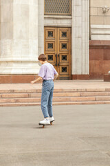 brunette teen with glasses with a skateboard on the streets of the city on a clear sunny day