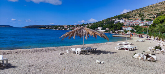 Beach view with umbrellas and sun loungers near the town of Trogir. Adriatic Sea and mountains. Dalmatia. Croatia. Europe - obrazy, fototapety, plakaty