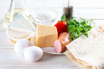 Ingredients for a healthy breakfast. Eggs, cheese, vegetables, bread, sausages, milk. Cooking omelet, roll, lavash