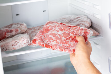The Man takes out a bag of frozen meat from the freezer in the kitchen at home. - obrazy, fototapety, plakaty