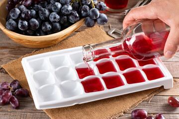 Pouring wine in ice cube tray on a wooden table. Frozen wine