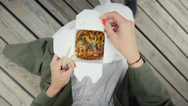 Top view on woman with take away box on her lap enjoy street food noodles. Delicious take away asian food. Food truck snacks or meal delivery with courier. Prepared food for business lunch break